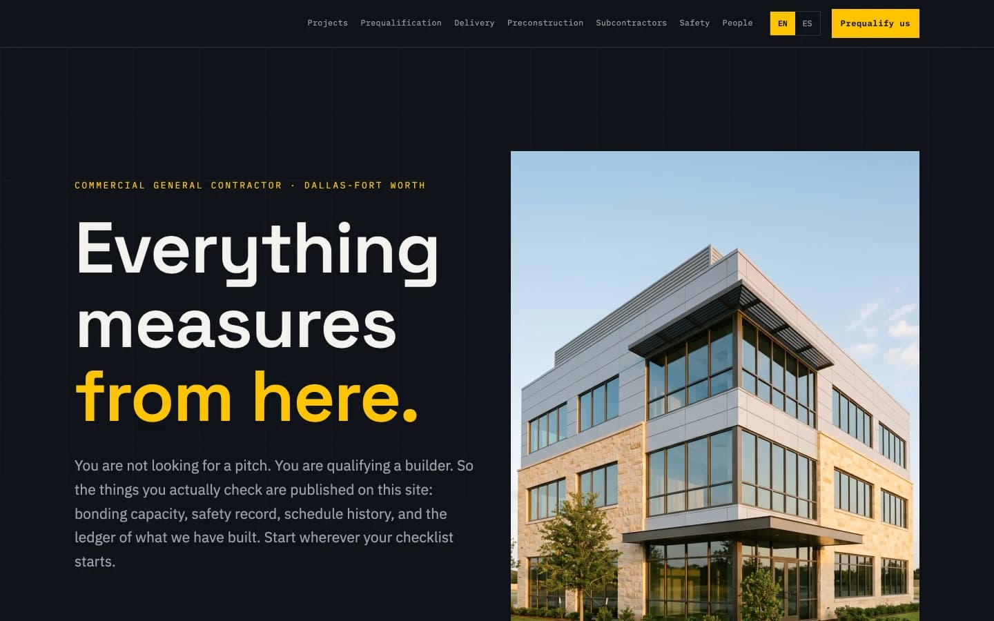 The Datum homepage hero: 'Everything measures from here.' in huge grotesk type over dark graphite, the last two words in safety yellow, above a mono kicker reading Commercial General Contractor, Dallas-Fort Worth, with a faint elevation grid behind the text and the datum-triangle mark in the nav.