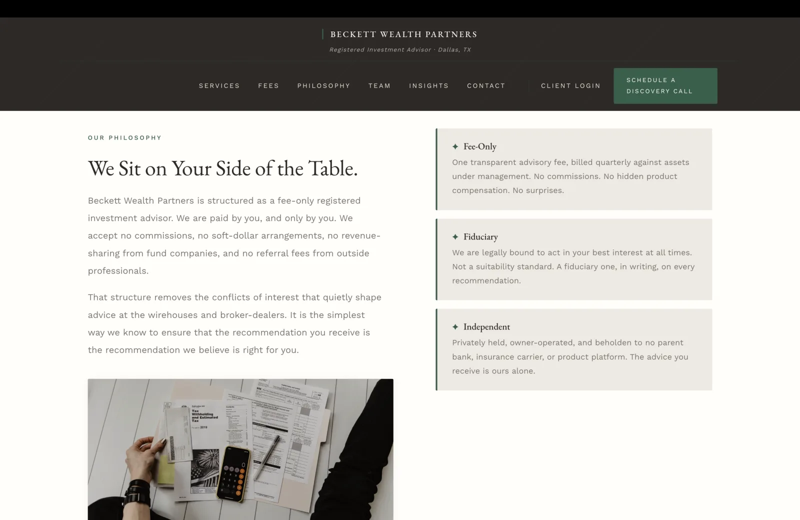 Sección de filosofía: un campo crema sereno con una maquetación partida. La columna izquierda lleva un rótulo verde pequeño en versales que dice OUR PHILOSOPHY, luego un titular serif alto 'We Sit on Your Side of the Table.' Siguen dos párrafos de cuerpo. Párrafo uno: 'Beckett Wealth Partners is structured as a fee-only registered investment advisor. We are paid by you, and only by you. We accept no commissions, no soft-dollar arrangements, no revenue-sharing from fund companies, and no referral fees from outside professionals.' Párrafo dos: 'That structure removes the conflicts of interest that quietly shape advice at the wirehouses and broker-dealers. It is the simplest way we know to ensure that the recommendation you receive is the recommendation we believe is right for you.' Bajo los párrafos, una fotografía editorial serena llena el cuadrante inferior izquierdo: una toma cenital de una mesa de madera blanquecina cubierta de documentos de finanzas personales en una sesión informal de planeación, incluido un instructivo del formulario 1040 titulado Tax Withholding and Estimated Tax for 2019, unas carpetas abiertas, un iPhone descansando sobre un bloc de notas adhesivas amarillo, una funda negra, y una mano en el borde inferior del cuadro. La columna derecha, sobre el mismo campo crema, lleva tres tarjetas horizontales apiladas cada una con un filete verde a la izquierda y un pequeño ícono de diamante verde. Tarjeta uno Fee-Only: 'One transparent advisory fee, billed quarterly against assets under management. No commissions. No hidden product compensation. No surprises.' Tarjeta dos Fiduciary: 'We are legally bound to act in your best interest at all times. Not a suitability standard. A fiduciary one, in writing, on every recommendation.' Tarjeta tres Independent: 'Privately held, owner-operated, and beholden to no parent bank, insurance carrier, or product platform. The advice you receive is ours alone.'