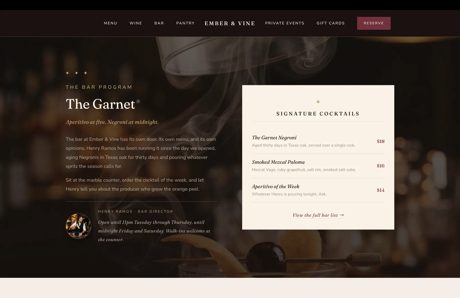 Bar Program section: a deep oxblood field with a smoky atmospheric photograph faded behind, showing curls of smoke and the silhouette of a coupe glass with a long peel garnish on the rail of a backlit bar. Foreground left column carries a centered three-diamond gold ornament, a small burgundy-on-oxblood eyebrow reading The Bar Program, then a large italic serif headline reading "The Garnet" with a small registered-trademark glyph. An italic gold tagline beneath reads "Aperitivo at five. Negroni at midnight." Two paragraphs of body copy follow: "The bar at Ember & Vine has its own door, its own menu, and its own opinions. Henry Ramos has been running it since the day we opened, aging Negronis in Texas oak for thirty days and pouring whatever spritz the season calls for." "Sit at the marble counter, order the cocktail of the week, and let Henry tell you about the producer who grew the orange peel." Below the paragraphs, a small circular portrait of Henry Ramos in a vest behind the bar, with a small caption beside reading Henry Ramos, Bar Director, plus an italic note about the bar staying open until 11pm Tuesday through Thursday and until midnight Friday and Saturday, walk-ins welcome at the counter. Right column on a calm cream card carries a small burgundy gold-trimmed header reading Signature Cocktails, then three cocktail rows separated by hairline rules. The Garnet Negroni, $18, aged thirty days in Texas oak, served over a single rock. Smoked Mezcal Paloma, $16, Mezcal Vago, ruby grapefruit, salt rim, smoked salt cube. Aperitivo of the Week, $14, whatever Henry is pouring tonight, ask. At the foot, an italic burgundy link reads "View the full bar list" with an arrow.